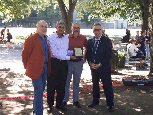 Ebrahim (Eby) Noroozi, winner of the inaugural Sustainable Labs Award, displays his plaque in a group photo with senior members of the McGill administration. From left to right: Associate Vice-Principal (Facilities Management and Ancillary Services) Robert Couvrette, Sustainable Labs Award winner Eby Noroozi, Associate Vice-Principal (Research & Innovation) Sylvain Coulombe, and Vice-Principal (Administration and Finance) Yves Beauchamp. The group is standing outside on the lower campus in the shade of a tree on a sunny fall day, and Eby is proudly displaying his award plaque.