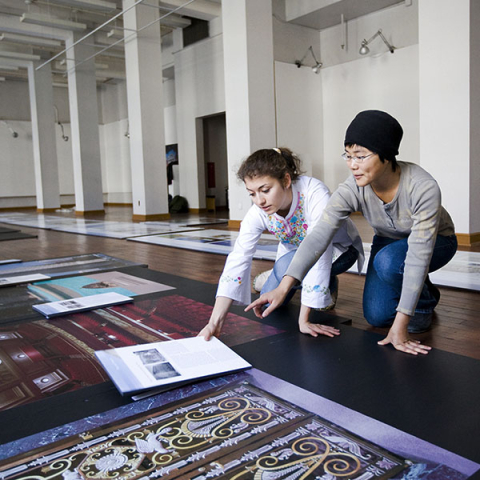 Young female student laying out photos of cultural artifacts with older woman in a gallery setting