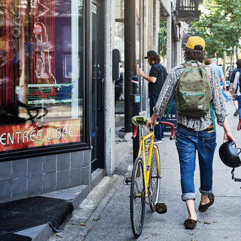 Photo of student wearing cap walking with yellow bike on city sidewalk
