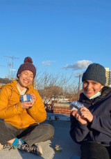 Three McGill students smiling and holding arepas on a roof in the evening sun.