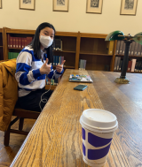 McGill student giving the thumbs up in a historic reading room in front of a to-go cup of coffee on a table