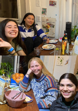 Four students smiling with pasta and wine on the table in front of them.