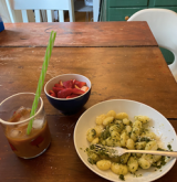 An iced coffee, bowl of strawberries, and bowl of pesto pasta on a table