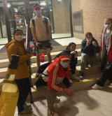 Six students in the lobby of a depanneur with a bottle of wine in the foreground