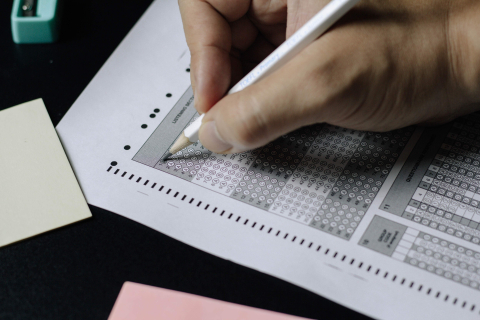 A hand holding a pencil, filling out a scantron exam sheet
