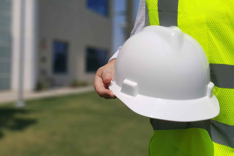 A construction worker holding a white hardhat, outside.