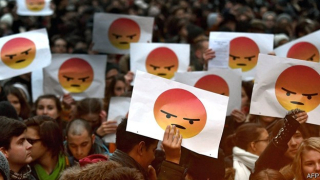 Crowd of people holding up signs with angry emojis