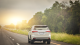 back of white car on road with sunset and trees on one side