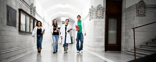 Four students in lab coats walk down the hall of the Strathcona Anatomy and Dentistry Building