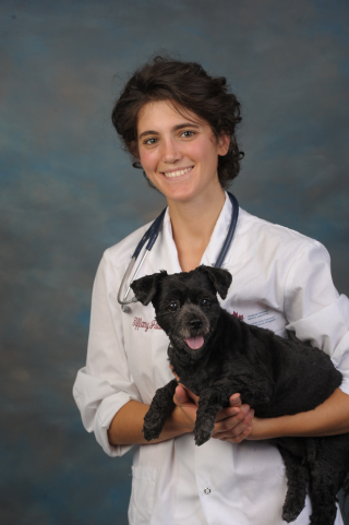 former McGill student Tiffany Gabriel-Bellantoni stands smiling holding a small dog, wearing a white lab coat