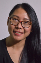 white background, Kim in a black top with an open smile, coloured rimmed glasses, long hair to one side