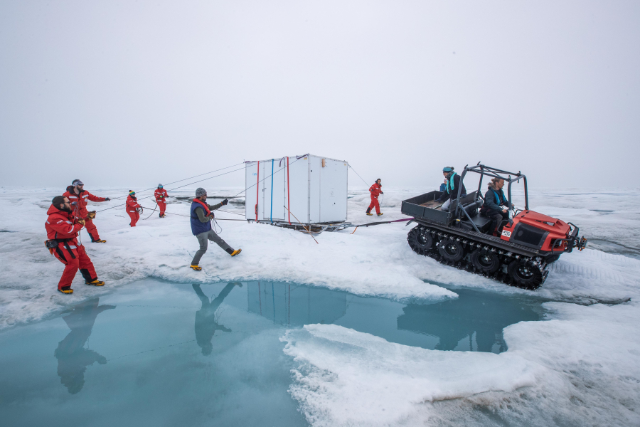 Several scientists in action to move a hut over melted sea ice