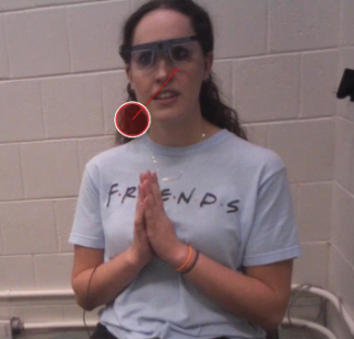 Jessica sitting in a chair wearing eye tracking glasses. There is a red dot near her chin that represents the pupil fixation of her interaction partner. 