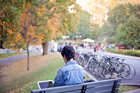 Student working on laptop on campus bench