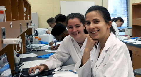 students in lab coats sitting at a bench