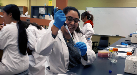 student in a lab coat pipetting liquid into a tube