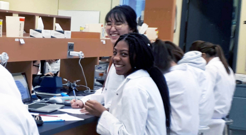 students in lab coats sitting at a bench