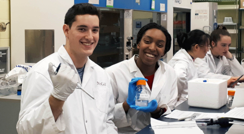 students in lab coats pipetting at a bench