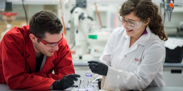 a male and female presenting students in a lab with a red and white coat looking over science tubes