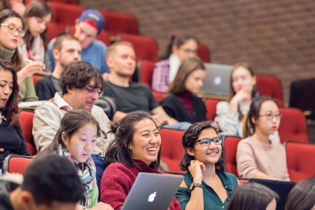 students in an auditorium facing the front and listening to a class
