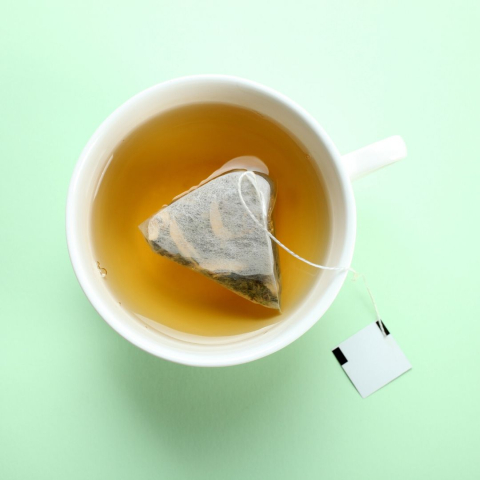 A mug with a tea bag floating in it, green background