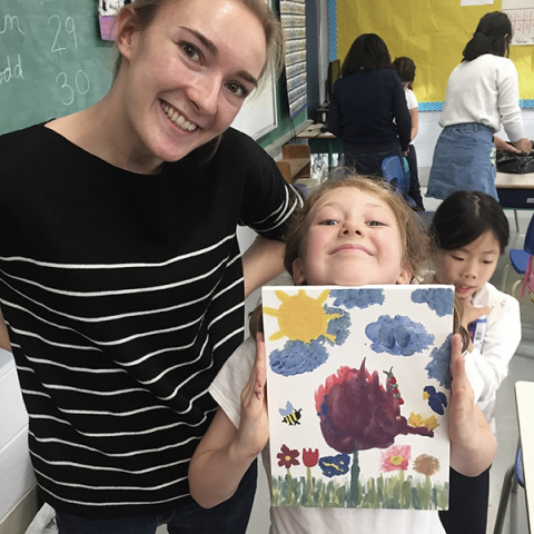 Mentor with young student who is proudly showing their painting to the camera.