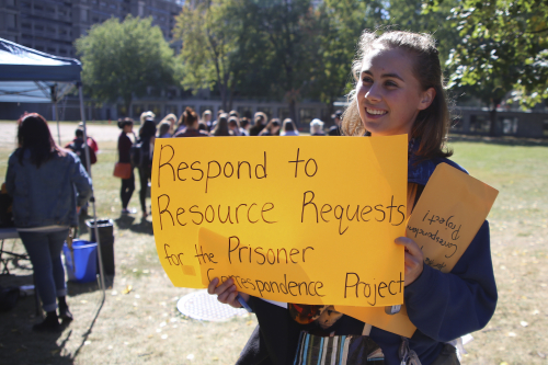 Student holds up sign promoting the Prisoner correspondence project during community engagemenbt day