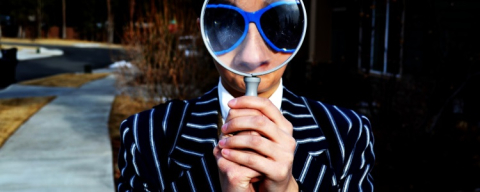Person with blue sunglasses holding a magnifying glass to their face
