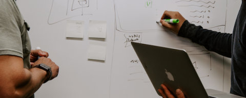 two people in front of a white board with laptop