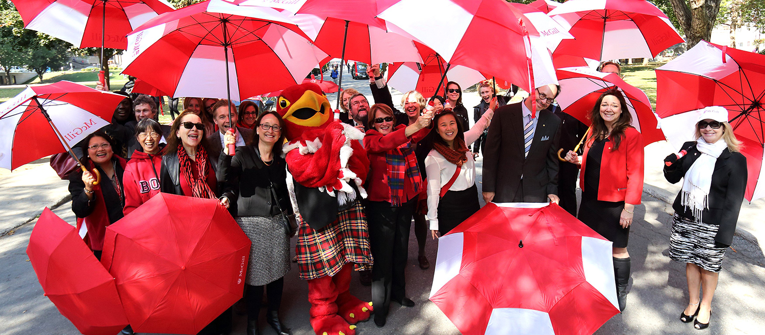 Similing McGill staff members posing with Marty the Martlette holding McGill umbrellas 