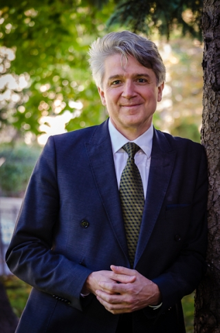 Professor Fabien Gélinas (a silver haired white man leans against a tree. He is wearing a blue suit). Photo by Lysanne Larose.