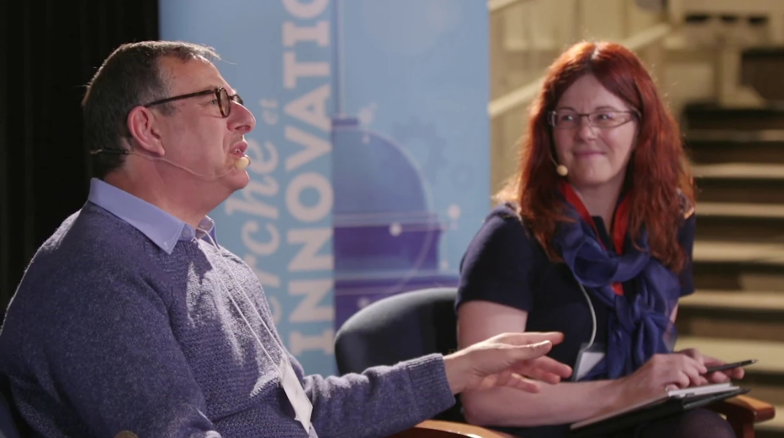 A man and a woman sitting at a table during a panel giving a presentation