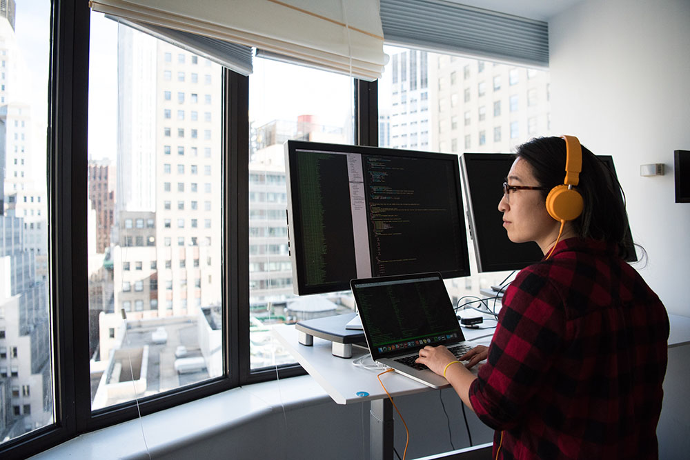 Person sitting in front of computer monitors and looking out the window