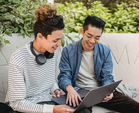 Two students sitting on a bench outside and looking at a laptop computer