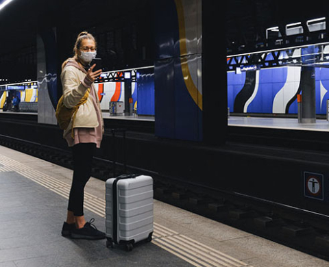 Woman on train platform with suitcase and cell phone