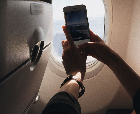 Image of hand holding cellphone and taking photo in airplane