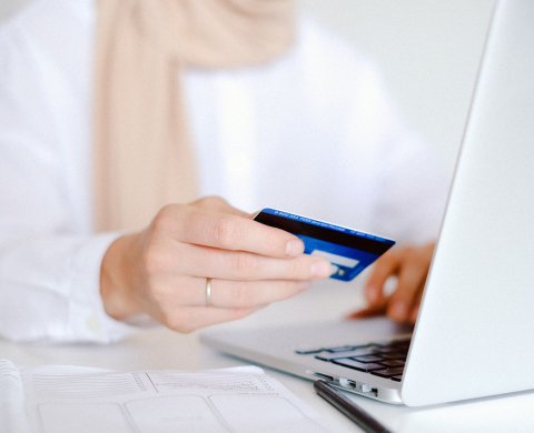Person sitting at laptop computer with credit card in hand