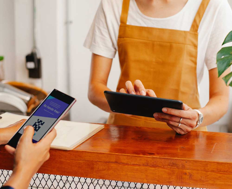 Customer paying with smartphone and staff wearing apron using tablet