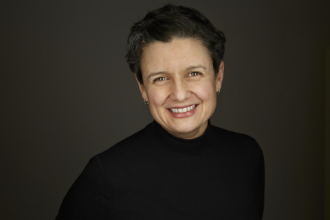 Andrea Warnick in front of a dark grey background, wearing a black sweater and smiling.