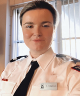 Woman in white shirt and tie uniform sitting in front of a window.