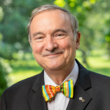 Dr. Gauthier in a bow tie in front of a green background of trees and grass.