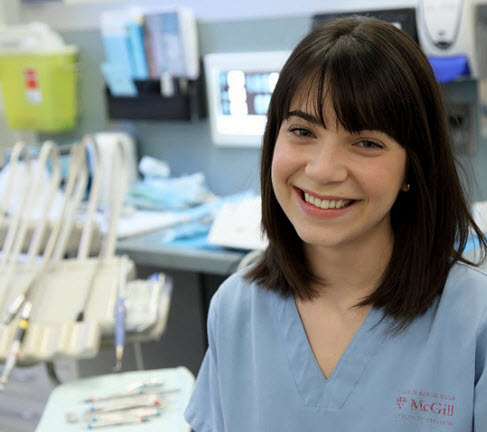 female dental student in dental clinic dressed in scrubs and smiling 