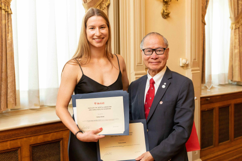 woman with long blond hair wearing a black dress, receiving a prize from an alumnus 