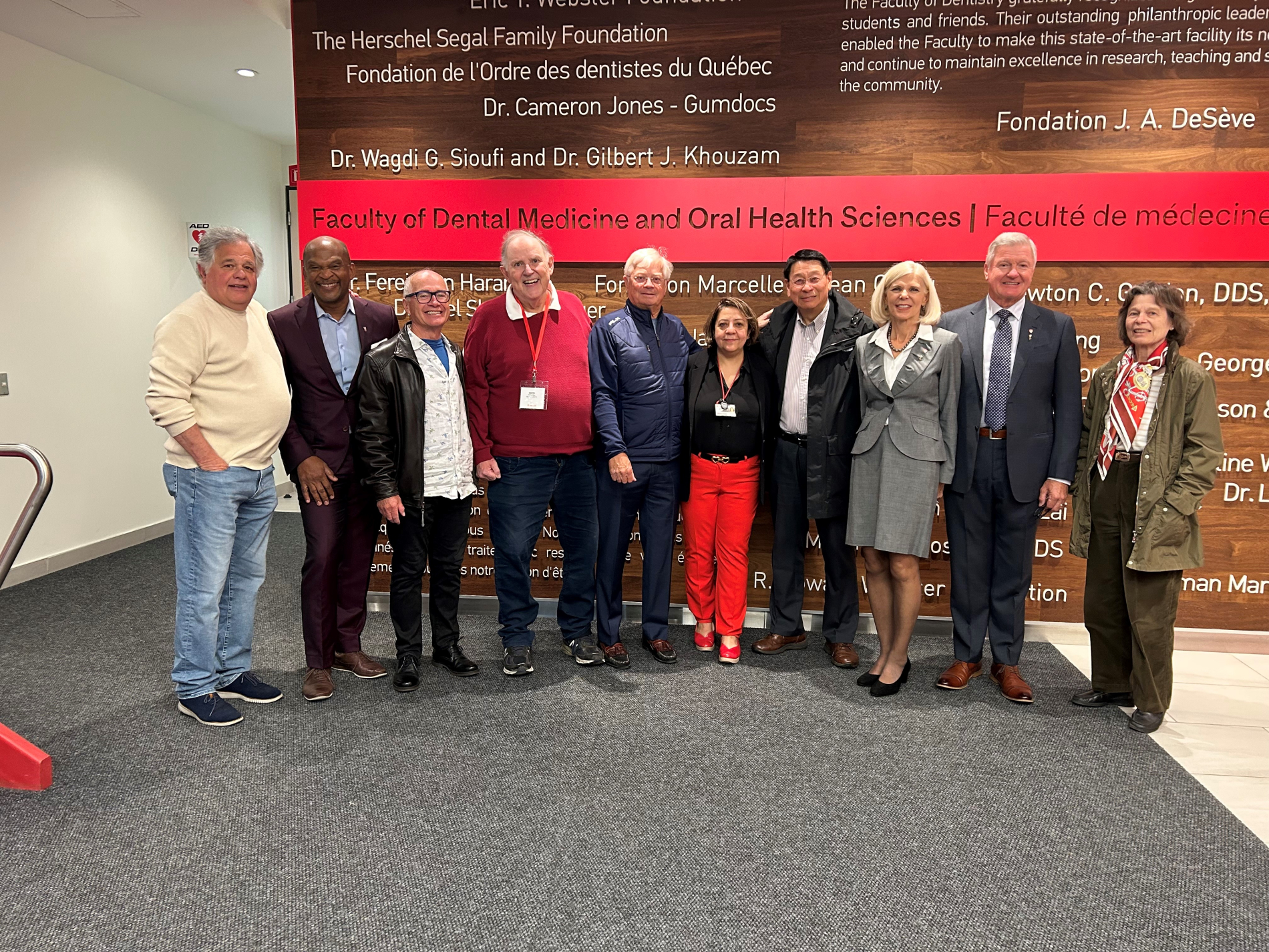 nine faculty alumni and the Dean standing in front of a wall with faculty name and donor names 