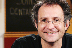 head shot of man with short brown hair and glasses wearing a black t-shirt