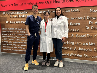 A man in blue medical scrubs, a woman wearing a white coat and a woman wearing a short white coat against a wood wall