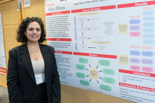 a woman with short curly brown hair wearing a black blazer standing next to a research poster 