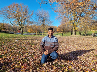 smiling young man kneeling in a park with fallen leaves all around