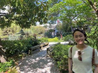 woman with short brown hair wearing a white short sleeve shirt standing in a garden 
