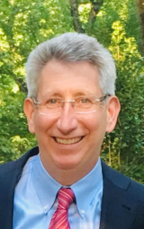 Irwin Fried wearing a navy blazer, blue shirt and red striped tie